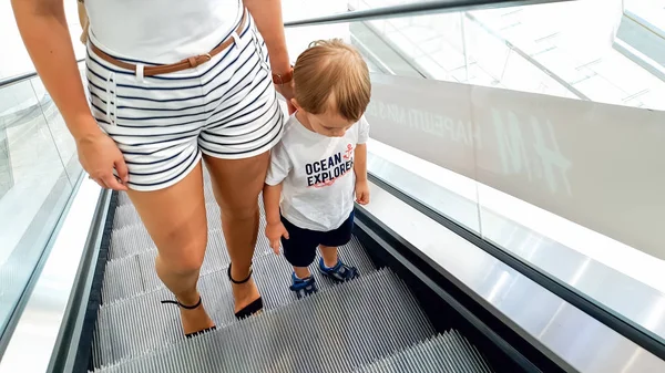 Fotografie mladé matky držící svého malého syna za ruku při jízdě na eskalátoru v nákupním středisku — Stock fotografie