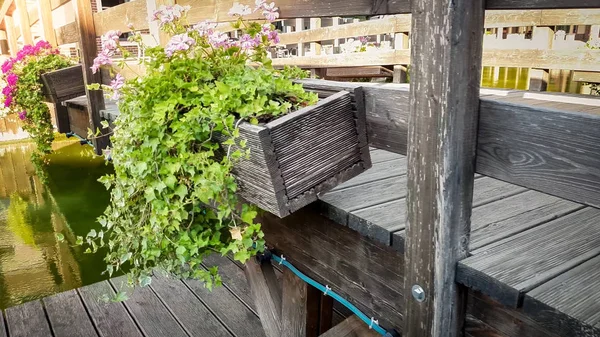 Closeup image of beautiful old wooden bridge with flowers growing in pots over calm river in european town — Stock Photo, Image