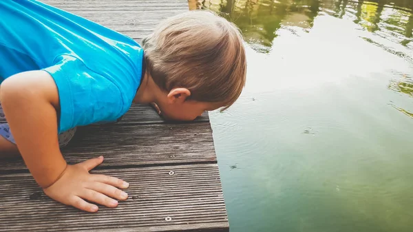 Gros portrait tonique d'adorable tout-petit garçon agenouillé à la rivière et regardant le parapente flottant à la surface du lac — Photo