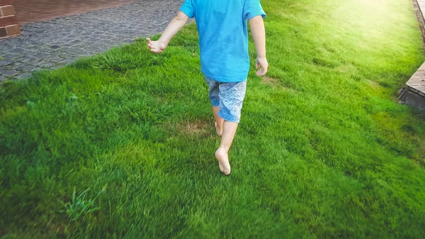 Close up image of 3 years old barefoot toddler boy running on hte fresh green grass at park — стоковое фото