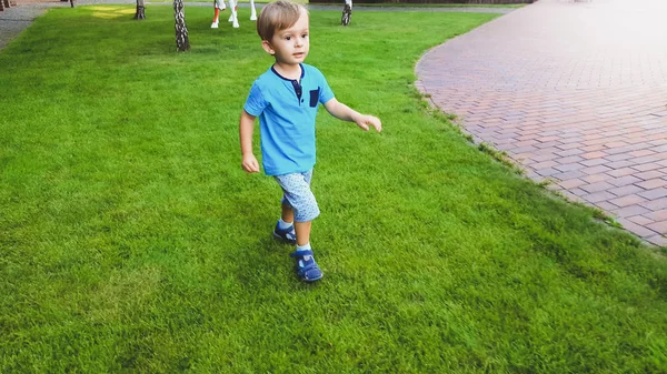 Portrait of smiling little boy running on grass lawn at park — Stock Photo, Image