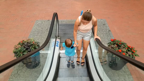 Alışveriş merkezi veya havaalanı terminalinde yürüyen merdiven üzerinde dururken annesini eliyle tutan küçük küçük çocuğun görüntüsü — Stok fotoğraf