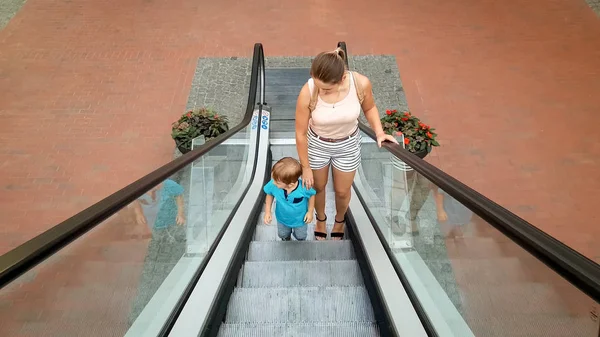 Photo de la jeune mère tenant son petit fils à la main alors qu'elle montait sur l'escalier roulant au centre commercial — Photo