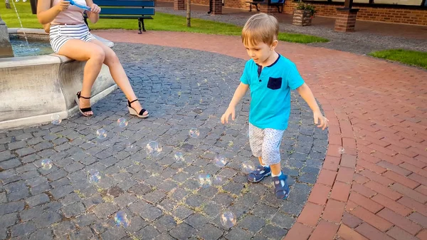 Petit garçon tout-petit de 3 ans courant après des bulles de savon colorées sur la place de la ville — Photo