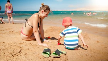 Fotoğraf 3 yaşındaki yürümeye başlayan çocuk bina kumdan kale ile genç anne okyanus plajı. Aile rahatlatıcı ve yaz tatili tatilinde eğlenmek.