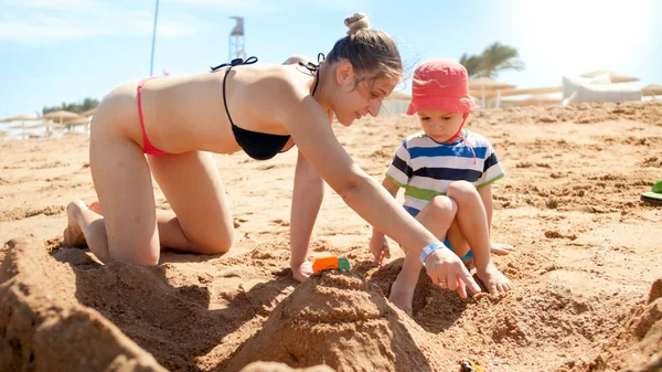 Foto de mãe com filho pequeno construindo castelo de areia na praia do mar. Pessoas a relaxar no oceano. Família descansando e se divertindo nas férias de verão . — Fotografia de Stock