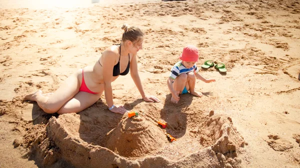 Portret młodej matki naucza jej 3-letniego syna malucha budynku zamków z piasku na plaży morskiej. Rodzinna relaksacyjne i zabawy na wakacjach wakacje. — Zdjęcie stockowe