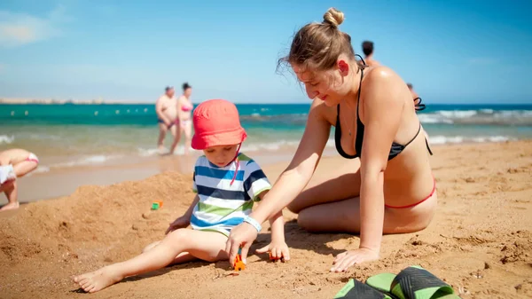 Photo of mother with little son building sand castle on the sea beach. People relaxing at ocean. Family resting and having fun on the summer holiday vacation. — Stock Photo, Image