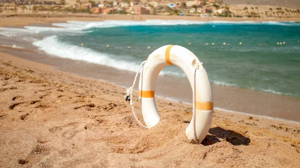 Beautiful image of white plastic life saving ring standing on the sandy sea beach at bright sunny day. Perfect shot to illustrate summer holiday vacation at ocean. — Stock Photo, Image