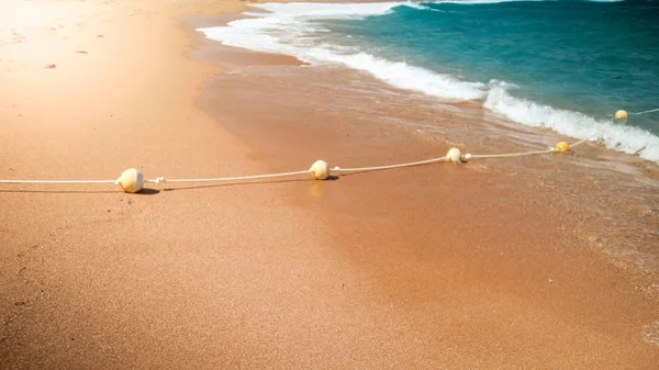 Imagem de close-up de bóias flutuantes de plástico conectadas em linha por corda deitada na praia do mar. Tiro perfeito para ilustrar férias de verão no oceano . — Fotografia de Stock
