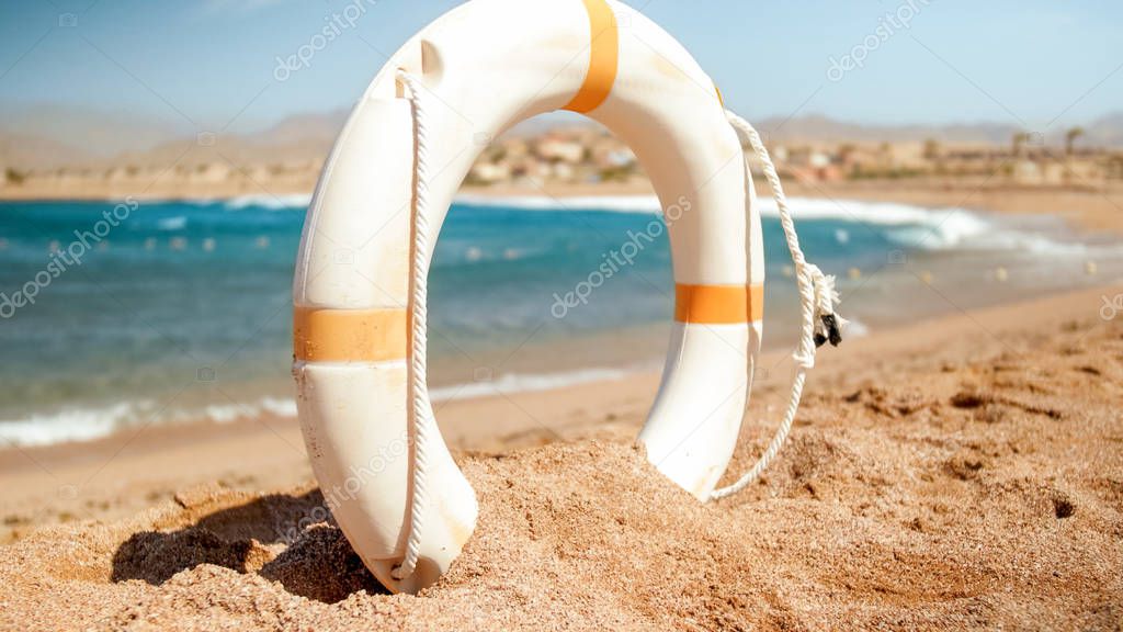 Closeup image of white plastic life saving ring on the sea beach at bright sunny day. Perfect shot to illustrate summer holiday vacation at ocean.
