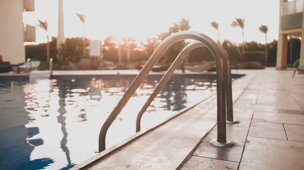 Closeup toned image of metal staircase railings in swimming pool against amazing sunset sky — Stock Photo, Image