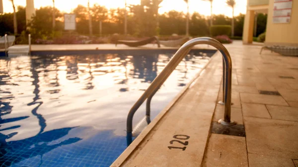 Closeup toned image of metal staircase railings in swimming pool against amazing sunset sky — Stock Photo, Image