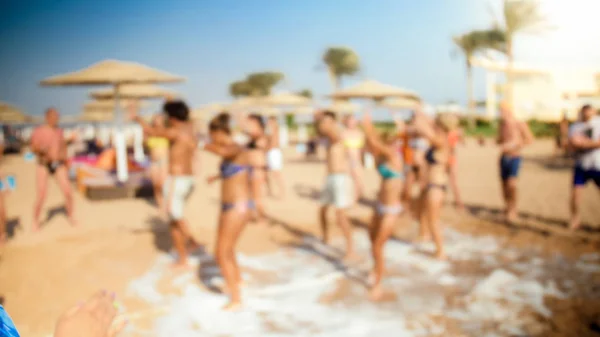 Imagem desfocada de jovens dançando na praia do mar na festa de discoteca de espuma de sabão . — Fotografia de Stock