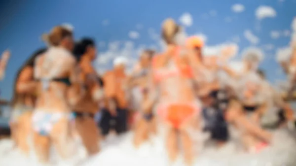 Imagem desfocada de pessoas felizes dançando juntas na praia. Amigos que têm espuma de sabão praia mar festa disco . — Fotografia de Stock