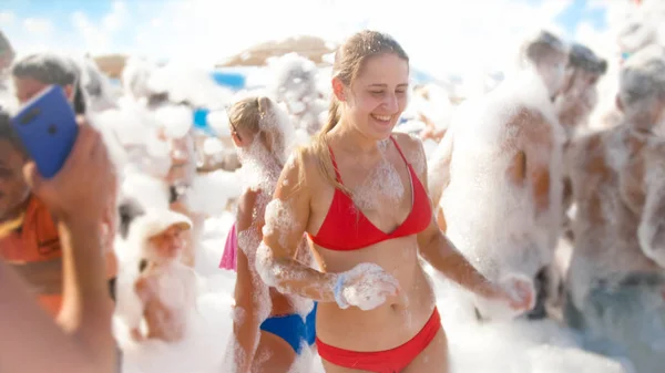 Closeup portrait of cheerful smiling young woman in red bikini dancing on the sea beach. Girl having fun on the soap foam disco party — Stock Photo, Image