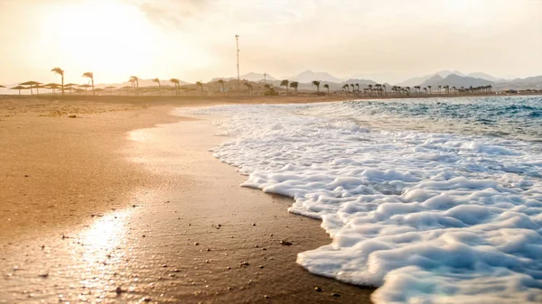 Foto de primer plano de las hermosas olas del océano azul rodando en la playa de arena contra el increíble atardecer — Foto de Stock
