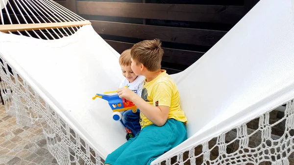 Image of teenage boy sitting and swinging in hammock with his younger little brother at house backyard — Stock Photo, Image