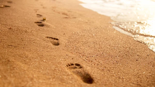 Gambar close-up jejak kaki di pasir basah pantai laut terhadap matahari terbenam langit — Stok Foto