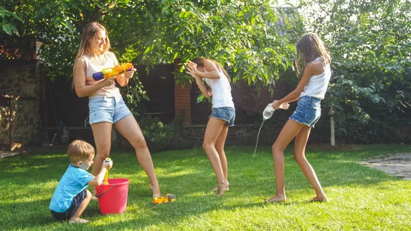Foto av lycklig skrattande familj stänk vatten med vattenkanoner och trädgårdsslang på bakgård. Människor som leker och har roligt på varma soliga sommardag — Stockfoto