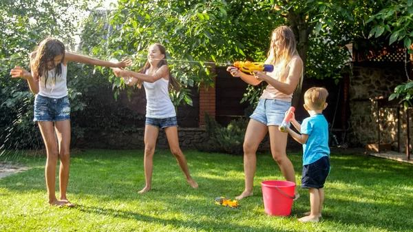 Funny foto av lycklig familj med barn leker och stänk vatten med vattenkanoner och trädgårdsslang på hot Sunny Day — Stockfoto