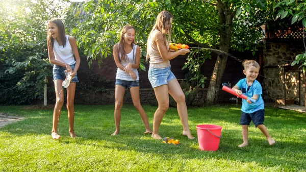 Mutlu neşeli çocukların görüntü wuth genç anne su tabancaları ve bahçe evi ile oynarken. Yaz aylarında dışarıda aile oynamak ve eğlenmek — Stok fotoğraf