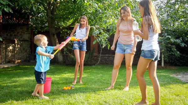 Legrační fotografie šťastné rodiny s dětmi, které hrají a stříkající vodu s vodními pistolemi a zahradní hadičkou za horkého slunného dne — Stock fotografie