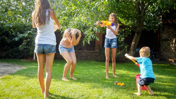 Fotografie šťastných dětí, které mají vodní pušky, bojují na zahradě u domu. Rodinná hra a zábava venku v létě — Stock fotografie