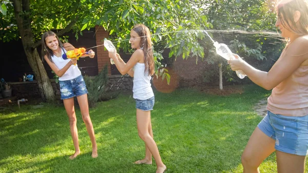 Imagen de niños felices jugando en el jardín del patio trasero de la casa con pistolas de agua y manguera de jardín. Familia jugando y divirtiéndose al aire libre en verano —  Fotos de Stock