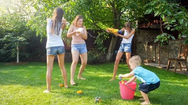 Vacker bild av lycklig skrattande familj med barn som har roligt på varm sommardag med vattenkanoner och trädgårdsslang. Familj leker och ha kul utomhus på sommaren — Stockfoto