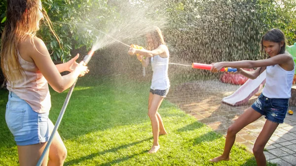 Image of happy cheerful children wuth young mother playing with water guns and garden house. Family playing and having fun outdoors at summer