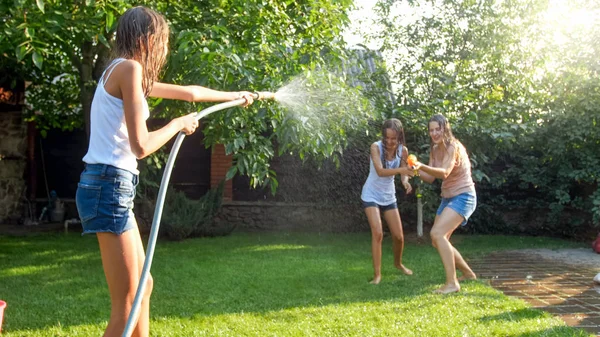Obraz szczęśliwego wesołego rodzinnego bawiąc się w ogrodzie podwórku. Ludzie rozpryskiwania wody z pistoletów wodnych i wąż ogrodowy. — Zdjęcie stockowe