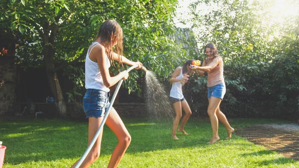 Foto van Happy Laughing familie spatten water met waterpistolen en tuinslang in de achtertuin. Mensen die spelen en plezier hebben op warme zonnige zomerdag — Stockfoto