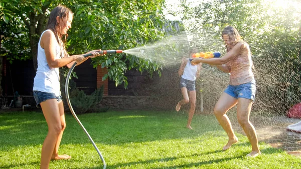 Imagen de niños felices jugando en el jardín del patio trasero de la casa con pistolas de agua y manguera de jardín. Familia jugando y divirtiéndose al aire libre en verano —  Fotos de Stock