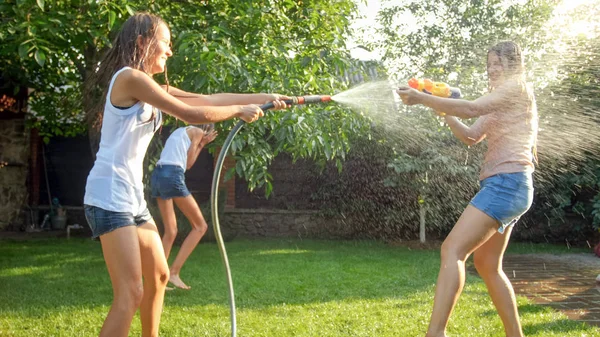 Imagem bonita de feliz família rindo com crianças se divertindo no dia quente de verão com pistolas de água e mangueira de jardim. Família brincando e se divertindo ao ar livre no verão — Fotografia de Stock