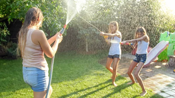 Imagem bonita de feliz família rindo com crianças se divertindo no dia quente de verão com pistolas de água e mangueira de jardim. Família brincando e se divertindo ao ar livre no verão — Fotografia de Stock