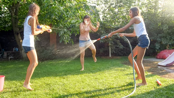 Foto av lycklig skrattande familj stänk vatten med vattenkanoner och trädgårdsslang på bakgård. Människor som leker och har roligt på varma soliga sommardag — Stockfoto