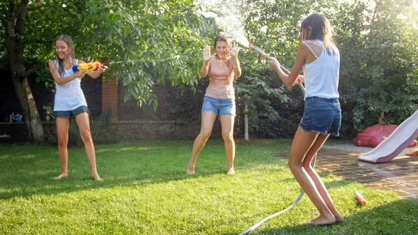 幸せな陽気な子供たちのイメージは、水の銃や庭の家で遊んで若い母親をうろつきます。夏に屋外で遊んだり楽しんだりする家族 — ストック写真
