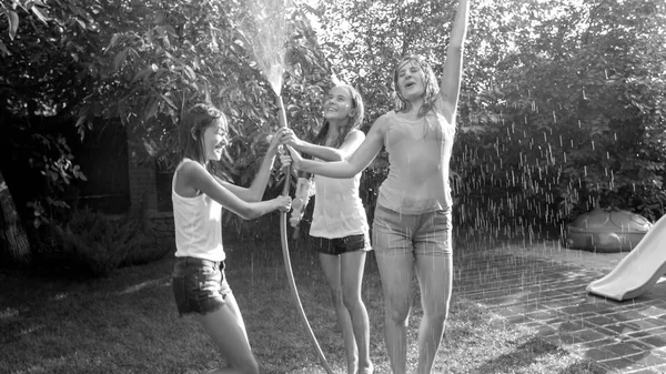 Plack e immagine bianca di ragazze ridenti allegre in vestiti umidi che ballano sotto acqua da tubo da giardino a giardino di cortile di casa. Famiglia giocare e divertirsi all'aria aperta in estate — Foto Stock