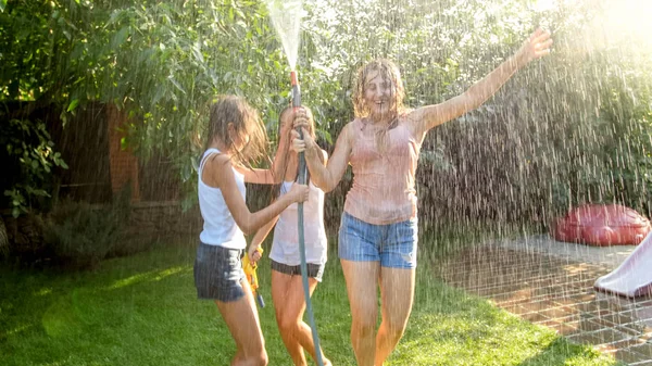 Foto de tres niñas adolescentes alegres bailando en el jardín del patio trasero udner manguera de agua del jardín —  Fotos de Stock