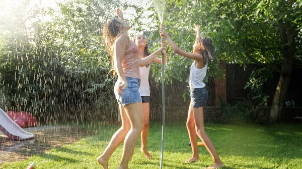 Foto de três adolescentes alegres dançando no quintal jardim udner jardim mangueira de água — Fotografia de Stock