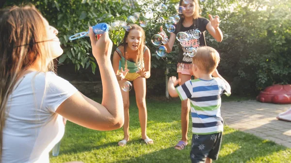 Смішний портрет щасливої веселої молодої сім'ї, що дме і катує мильні бульбашки в саду на подвір'ї — стокове фото