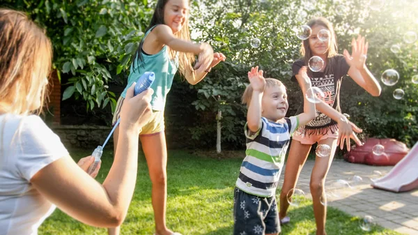 Photo of happy laughing children blowing and cathcing soap bubbles at house backyard. Family playing and having fun outdoors at summer — Stock Photo, Image