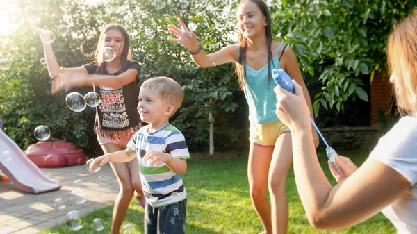 Retrato engraçado de feliz alegre jovem família soprando e catando bolhas de sabão em casa quintal jardim — Fotografia de Stock