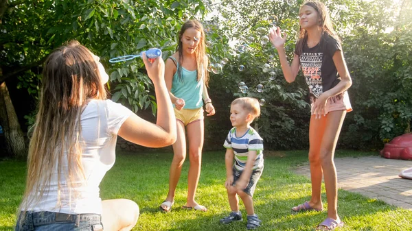 Photo of happy laughing children blowing and cathcing soap bubbles at house backyard. Family playing and having fun outdoors at summer — Stock Photo, Image