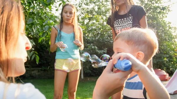 Funny portrait of happy cheerful young family blowing and cathcing soap bubbles at house backyard garden — Stock Photo, Image