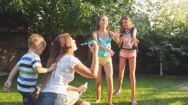 Photo of happy laughing children blowing and cathcing soap bubbles at house backyard. Family playing and having fun outdoors at summer — Stock Photo, Image