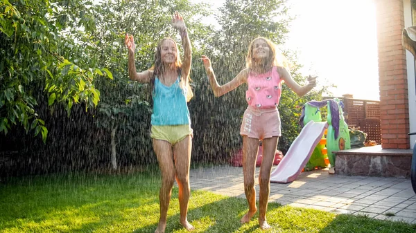 Foto di bambini felici ridendo in vestiti bagnati che saltano e ballano sotto pioggia calda a giardino. Famiglia giocare e divertirsi all'aria aperta in estate — Foto Stock