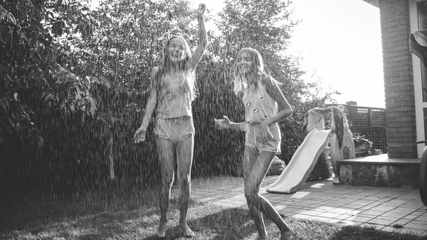 Zwart-wit beeld van twee gelukkig lachende meisjes genieten van warme zomer regen in de tuin. Familie spelen en plezier buitenshuis in de zomer — Stockfoto