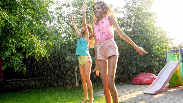 Photo d'enfants heureux riant en vêtements humides sautant et dansant sous la pluie chaude au jardin. Jouer en famille et s'amuser à l'extérieur en été — Photo